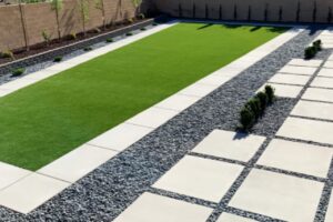 Close-Up Of Artificial Grass Installed By Green America Tree &Amp; Landscaping In Las Vegas, Bordered By Pavers And Decorative Landscape Rock.