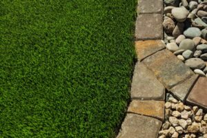 Close-Up Of Artificial Grass Installed By Green America Tree &Amp; Landscaping In Las Vegas, Bordered By Pavers And Decorative Landscape Rock.