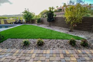 Decorative River Rock Landscaping Paired With Artificial Grass, Pavers, And Desert Plants In A Low-Maintenance Las Vegas Backyard.
