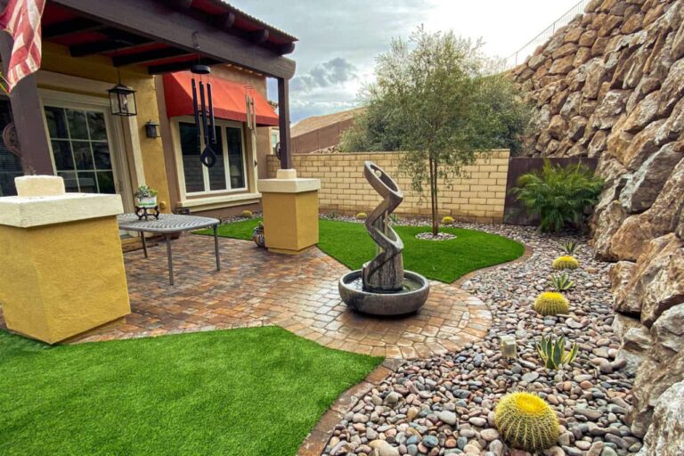 Backyard Landscape Featuring Decorative Rock Borders Around Artificial Grass And Trees For A Clean Desert-Friendly Design In Las Vegas.
