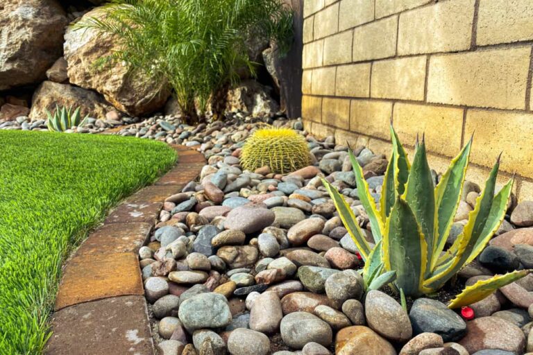 Decorative River Rock Landscaping With Agave, Cactus, And Artificial Grass For A Water-Smart Las Vegas Yard Design.