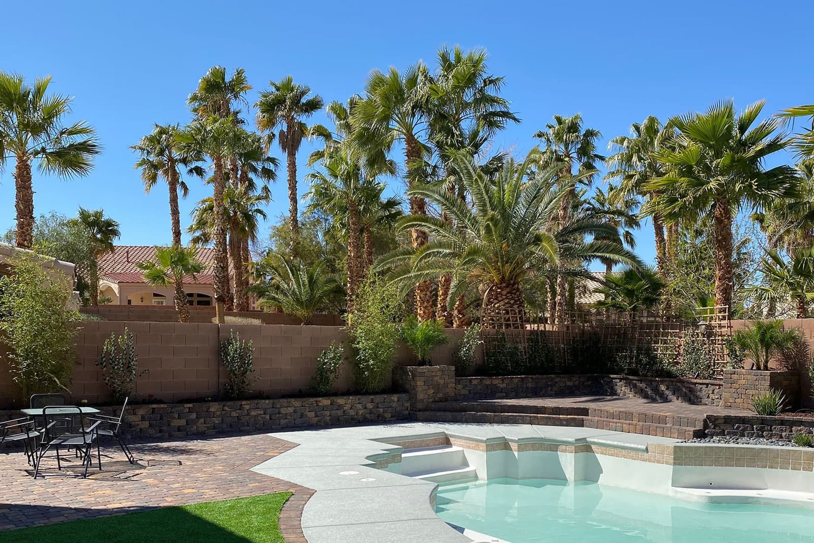 A Las Vegas Home Backyard Pool Area With Pavers, Hardscape Elements And Pruned Palm Trees.